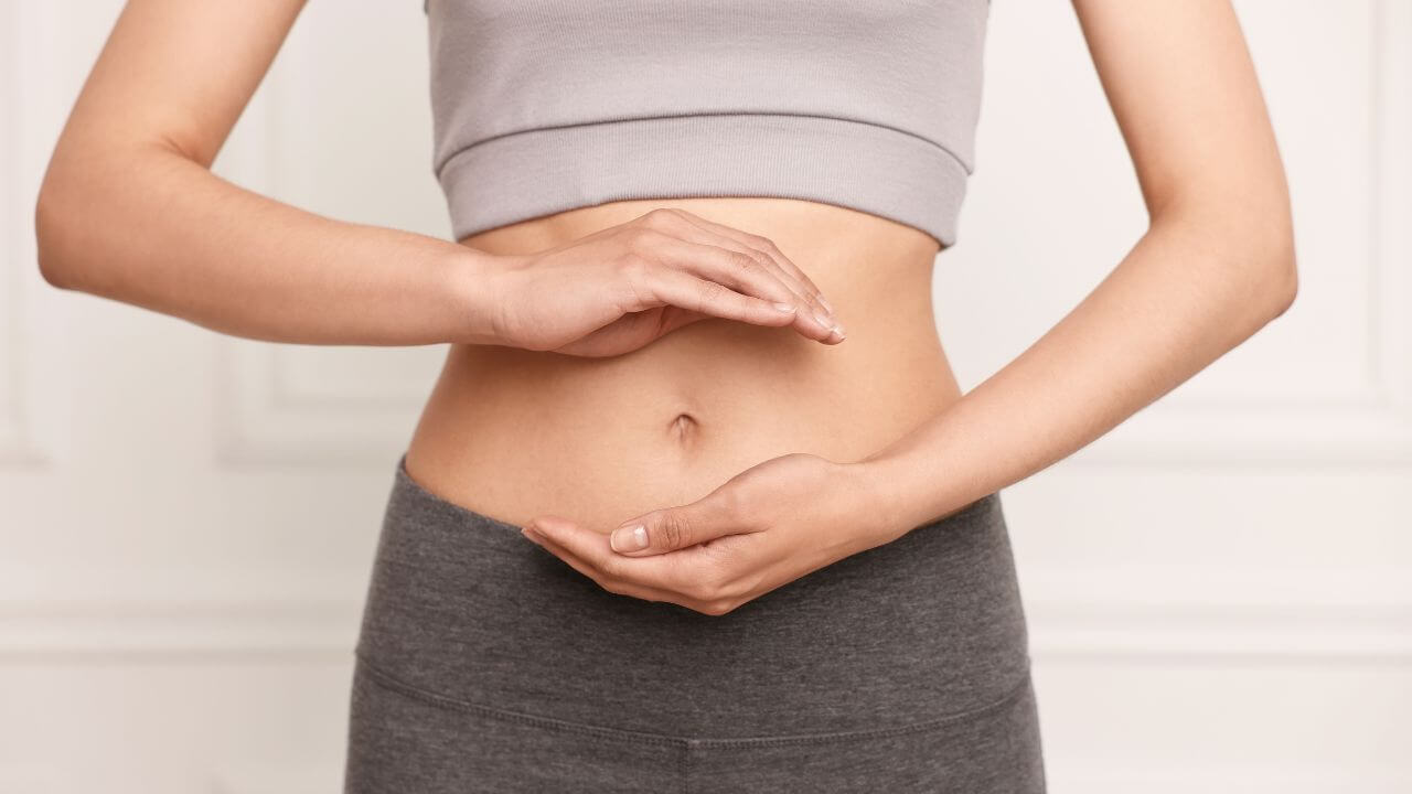 Frau zeigt auf Bauch, symbolisiert die Verdauung - Unser Körper arbeitet rund um die Uhr.