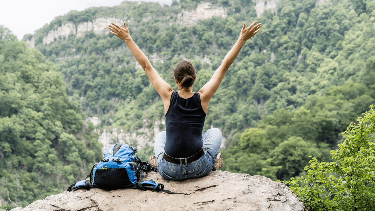Eine Frau sitzt mit ausgestreckten Armen  in der ruhigen Natur