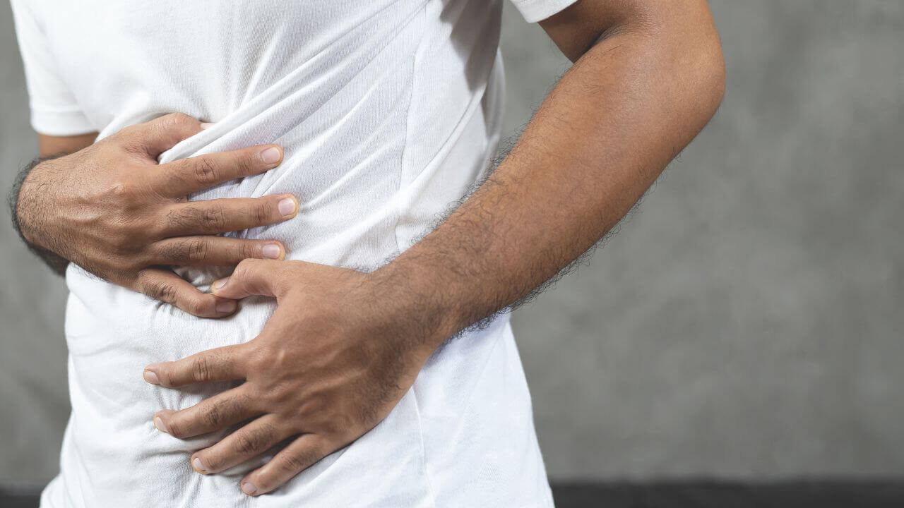 Mann mit Hands auf dem Bauch, der Schmerzen oder Unbehagen im Bereich des Darms zeigt.