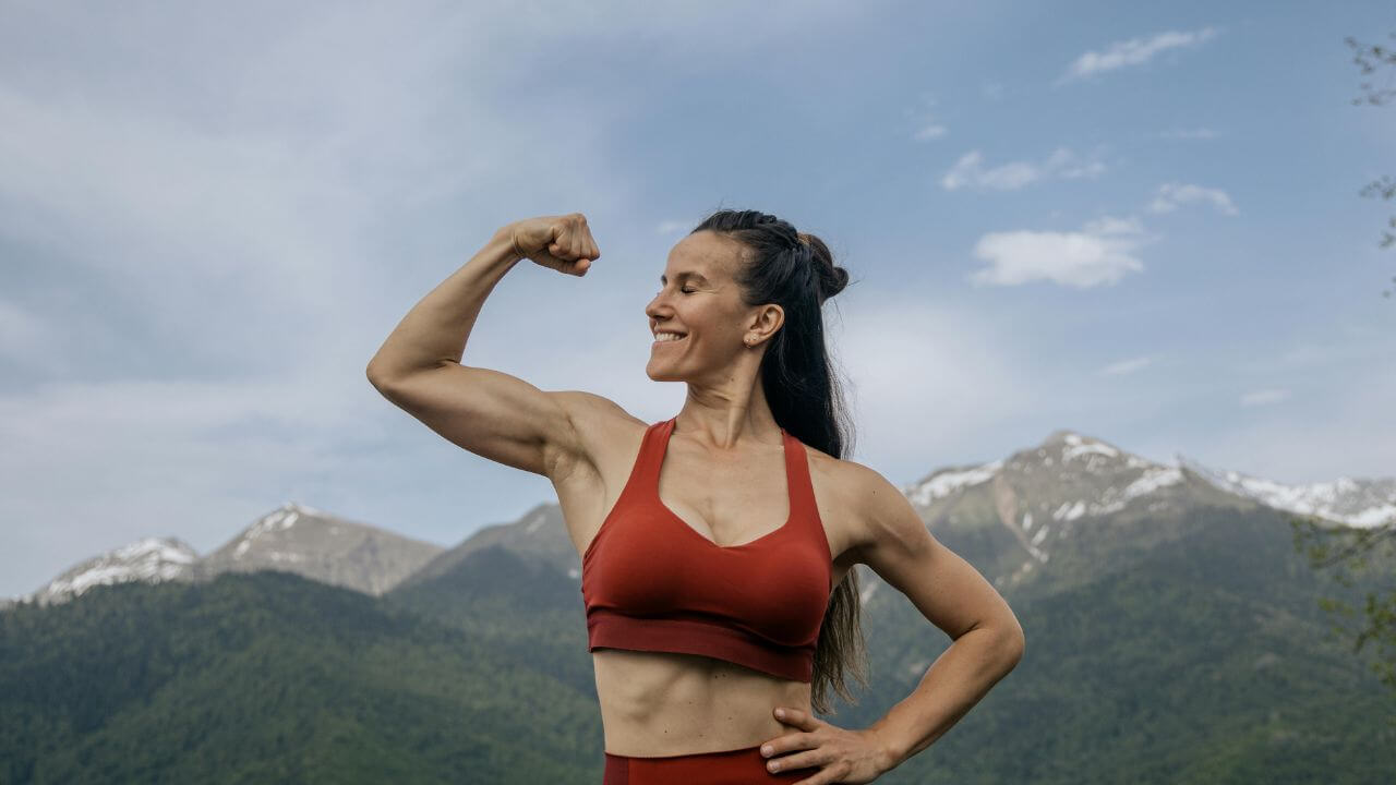 Verstehe deine Muskeln besser! Starke Frau zeigt Muskeln vor Berglandschaft.
