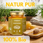 Bio honeycomb honey by Vitalplant in a glass jar, surrounded by honeycomb and a wooden spoon.